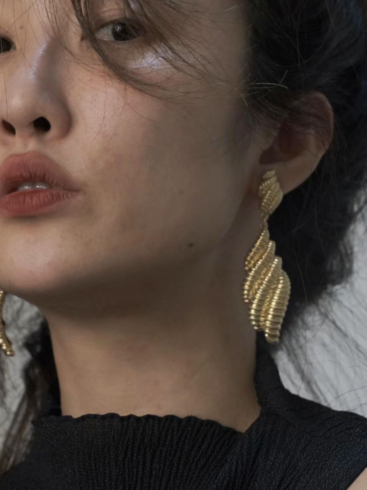 The simple black outfit is paired with sleek gold conch earrings for a modern, minimalist aesthetic.