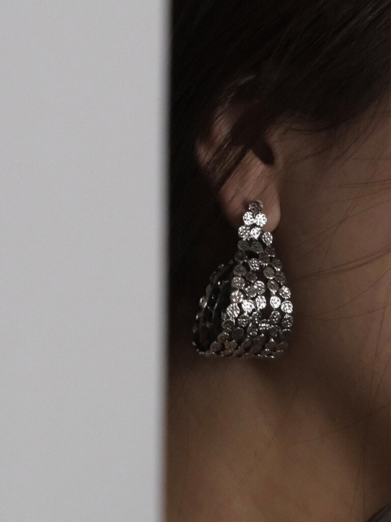 Silver hammered earrings with a teardrop-shaped hollow hammered design, combining metallic luster with 3D texture, showing a retro and chic style when worn.