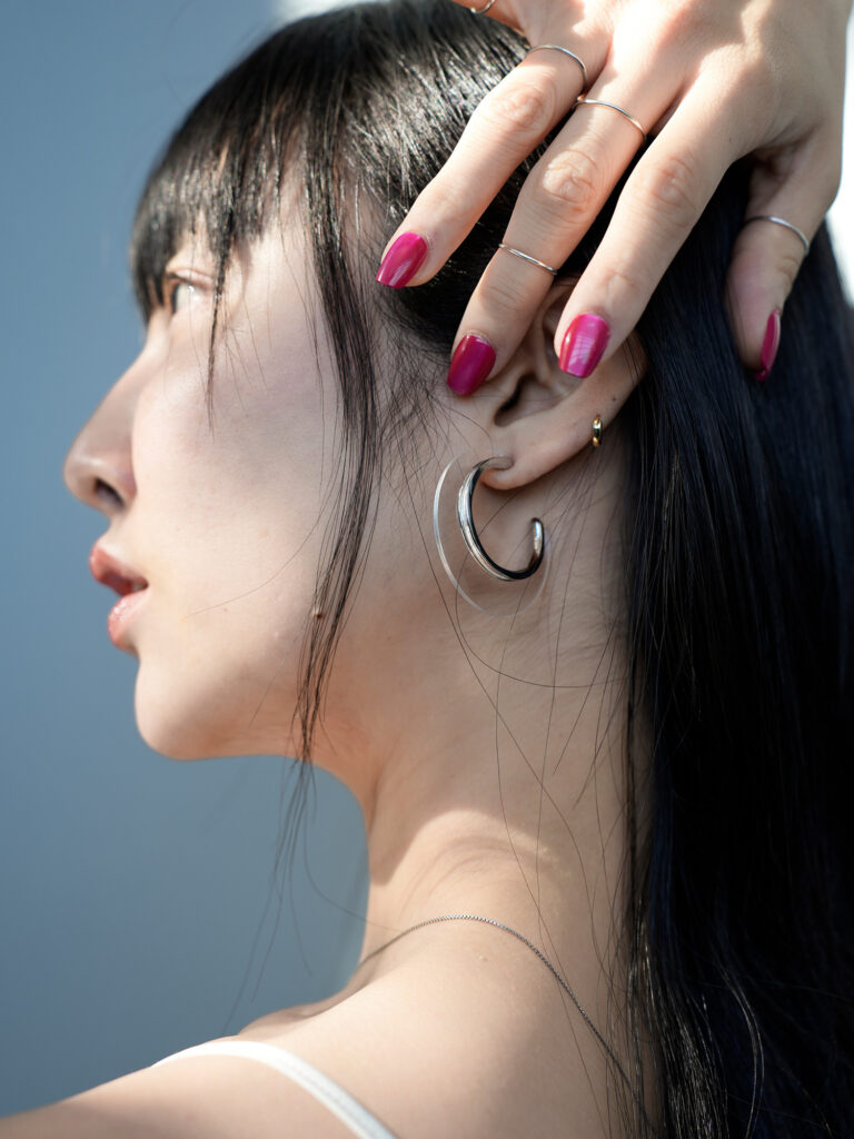 Transparent acrylic crescent earrings are stacked with metal rings and worn on the ears, showing a fashionable transparent water-like texture in the light and shadow.